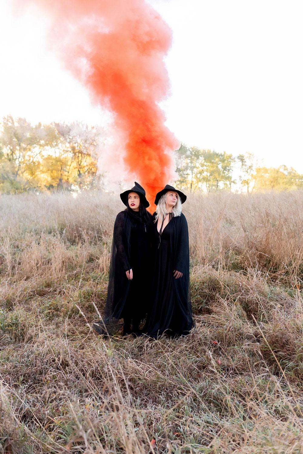Two ladies in black cloaks stand in a field with red smoke billowing above them at sunset in strathroy ontario.