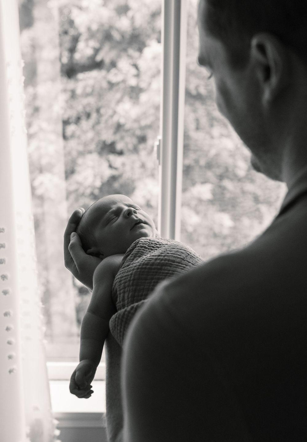 Silhouetted figures holding baby while standing near window.