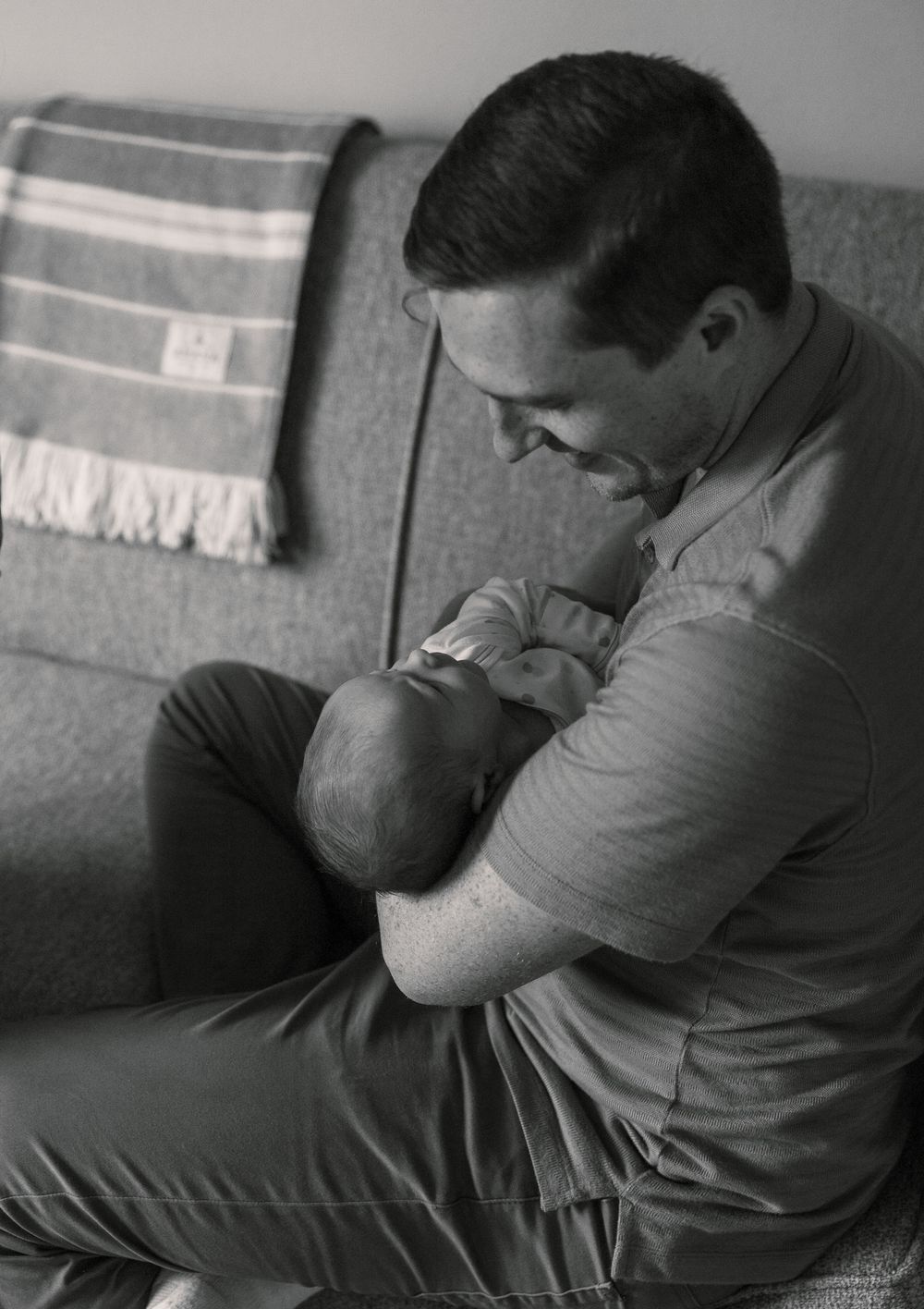 Black and white image of tender moment between parent and baby on couch.