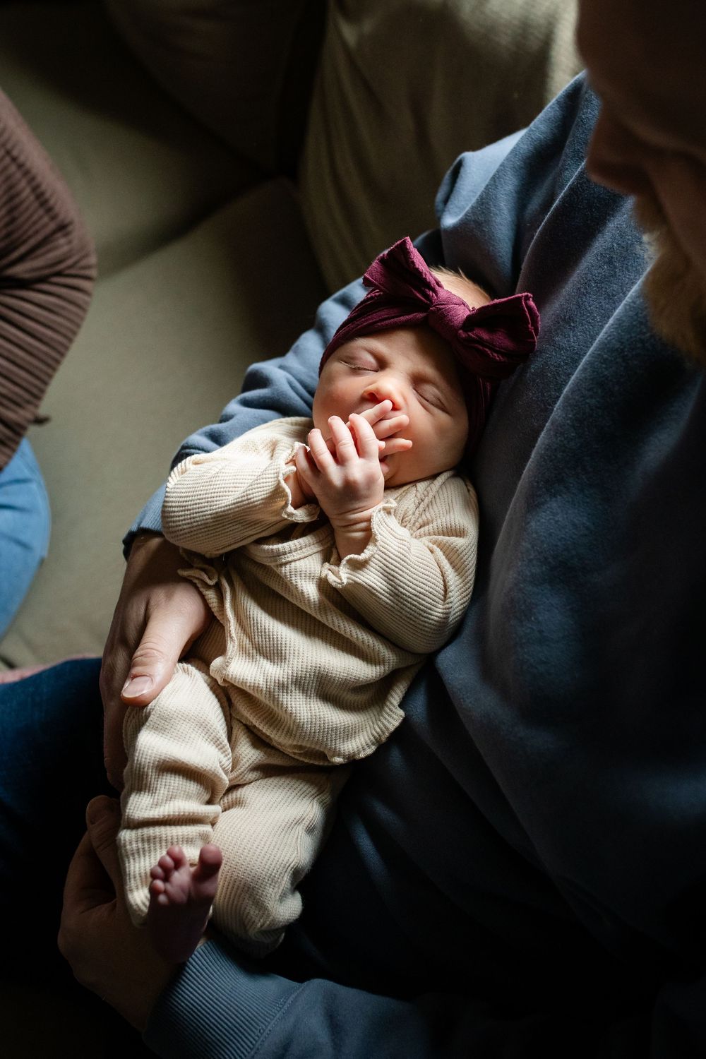 Sleeping newborn baby wrapped in cream colored knit blanket being held in dark fabric.