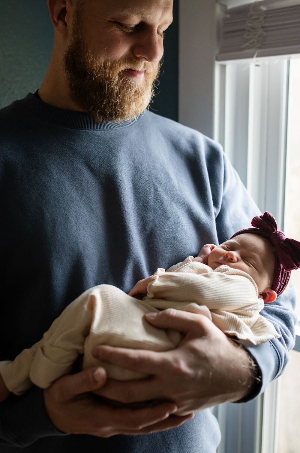 A tender moment as a person in a gray sweater cradles and looks down at a newborn baby wrapped in white blankets.