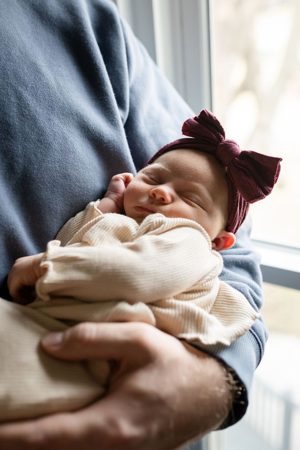 A series of photos showing a sleeping newborn baby being cradled in someone's arms wearing a blue sweater.