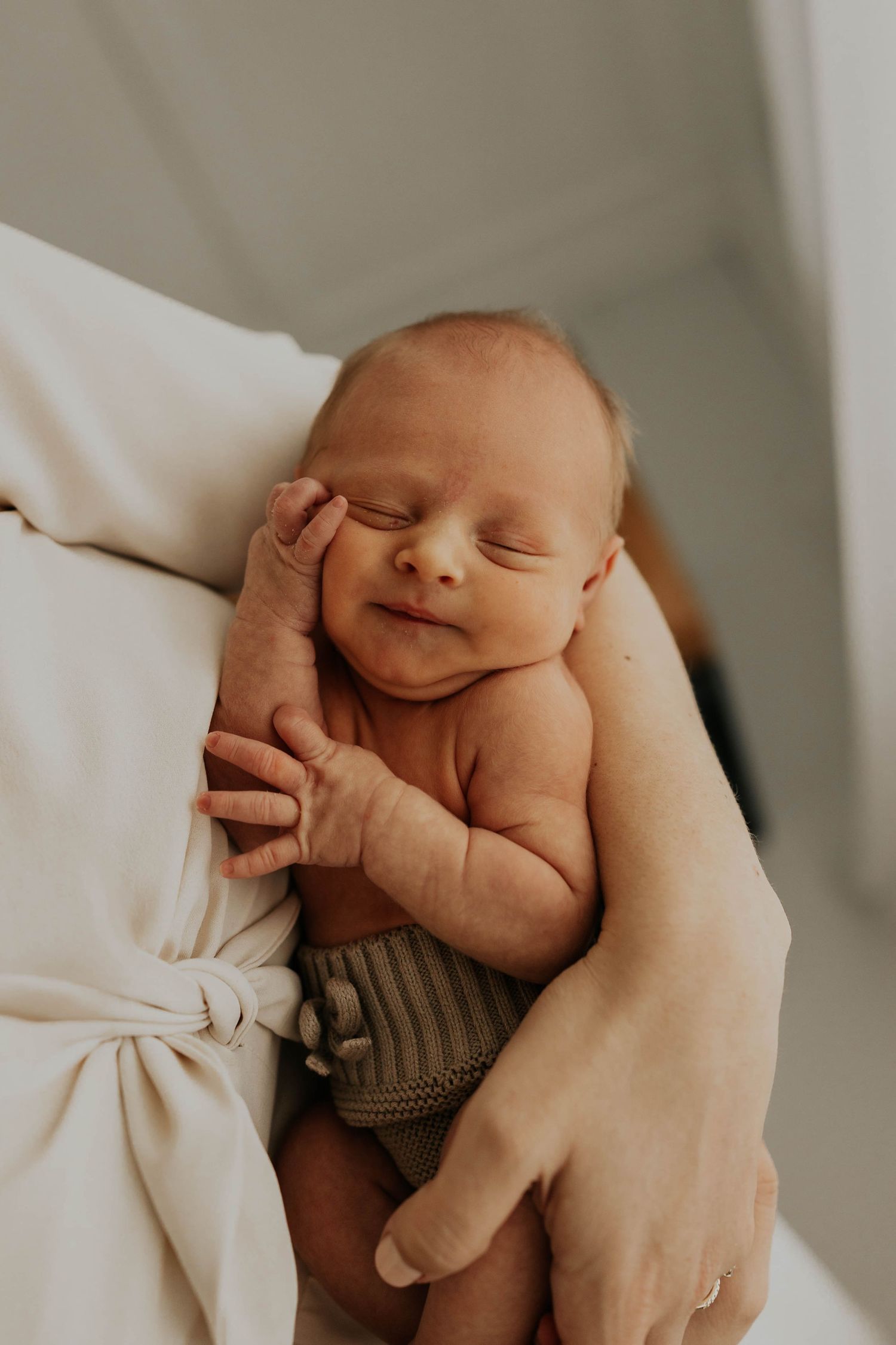 Newborn baby sleeping peacefully on soft white bedding in natural light.