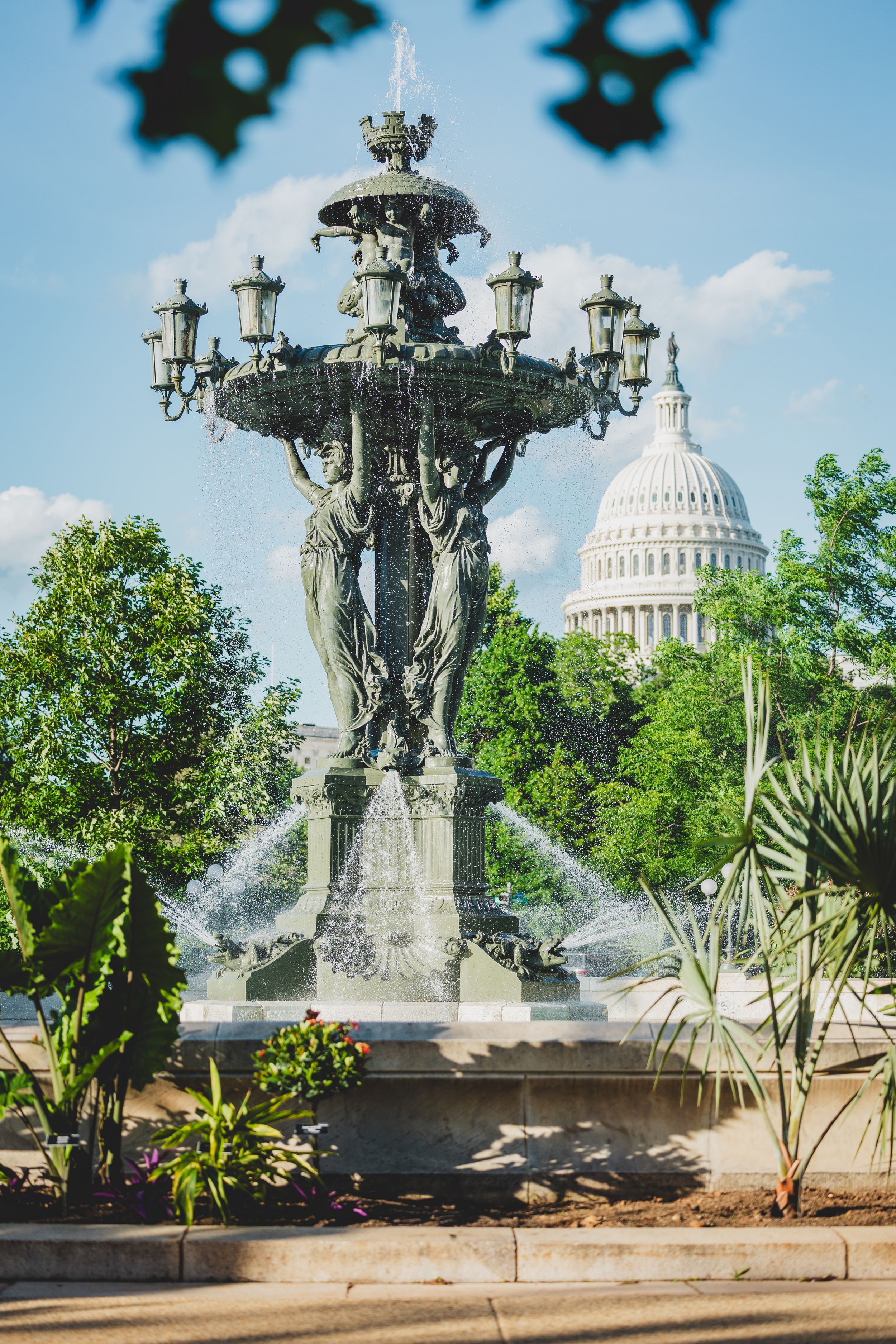 Ornate fountain with water jets and lamp posts stands in front of the US Capitol Building dome in Washington DC.