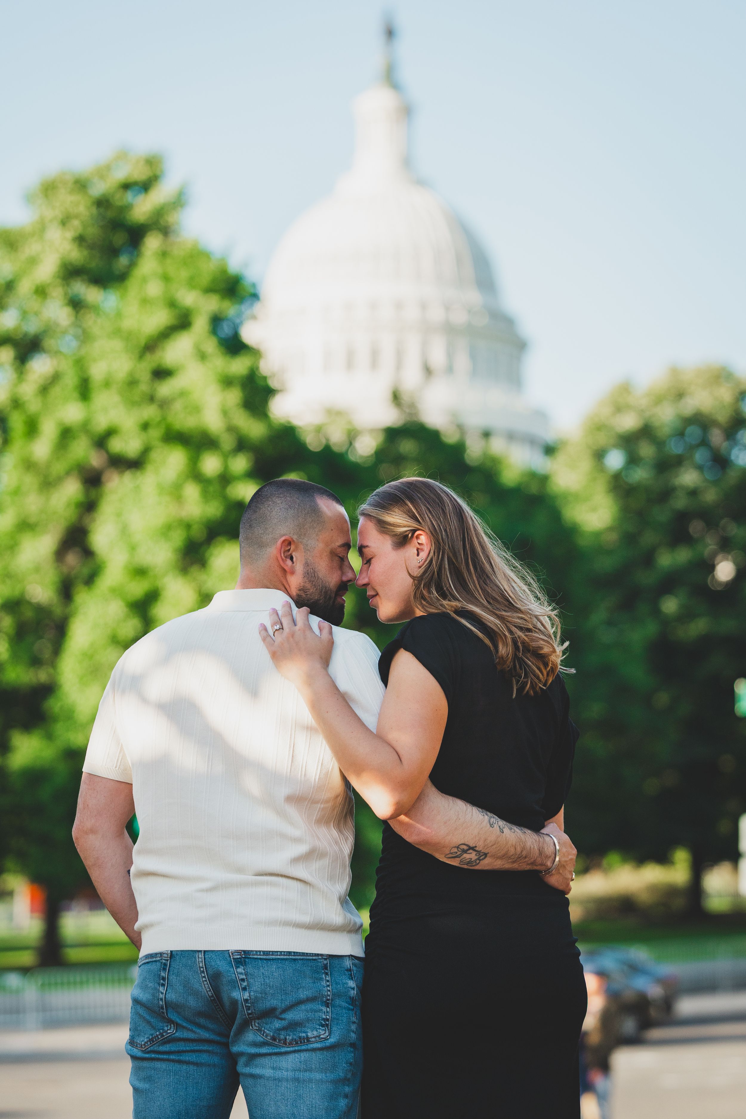 A couple shares a romantic moment together in front of the United States Capitol building on a sunny day.