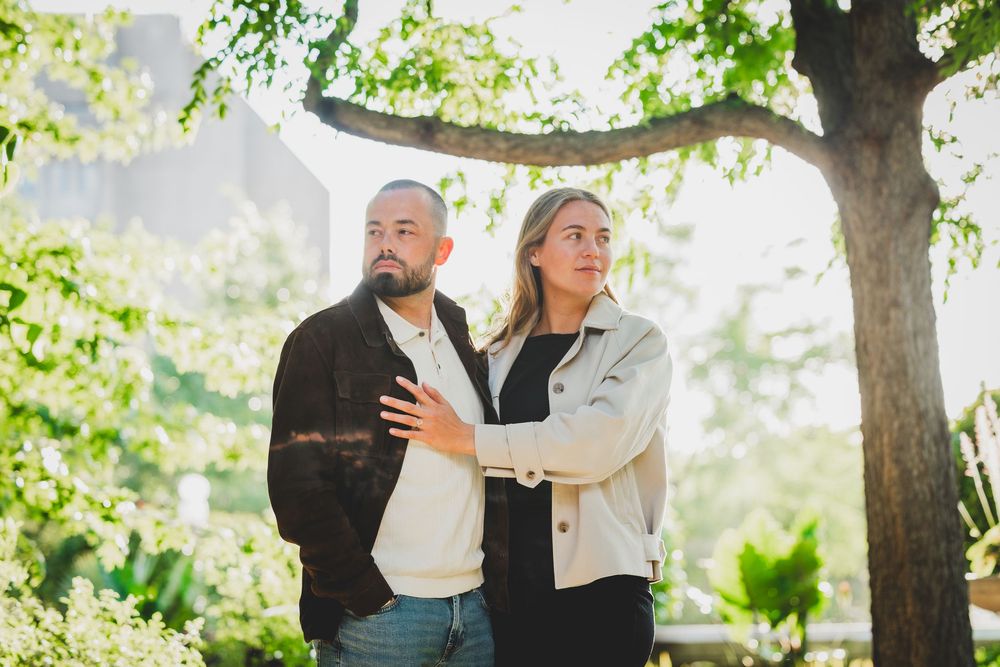 A couple shares a joyful moment dancing together outdoors under sunlit trees in a natural setting.