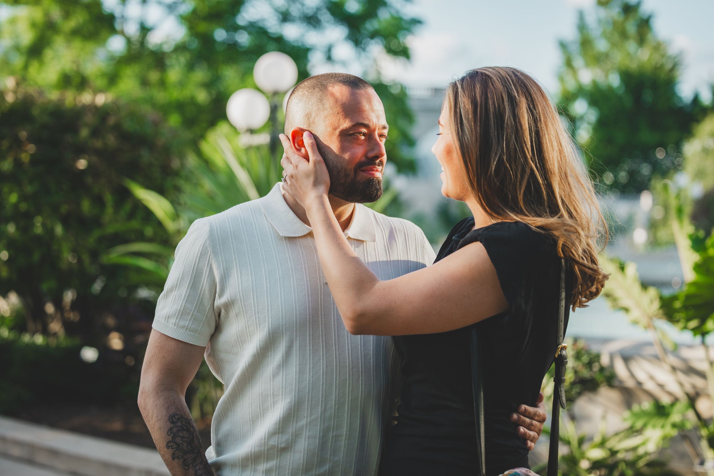 A couple embraces outdoors in a sunlit garden setting while sharing an intimate moment together.