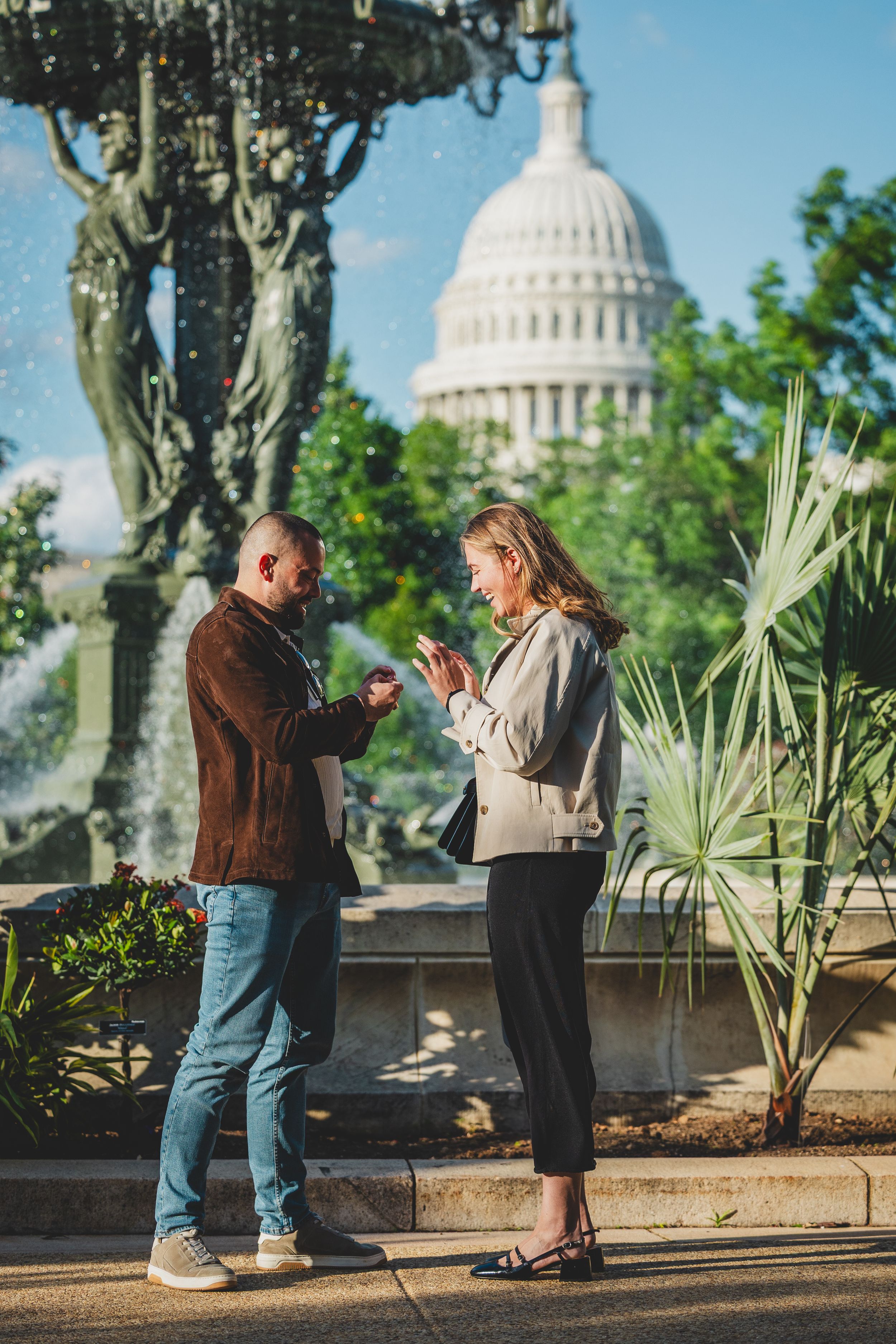 Two people checking their phones while standing near the US Capitol building in Washington DC with decorative lamp post and plants.