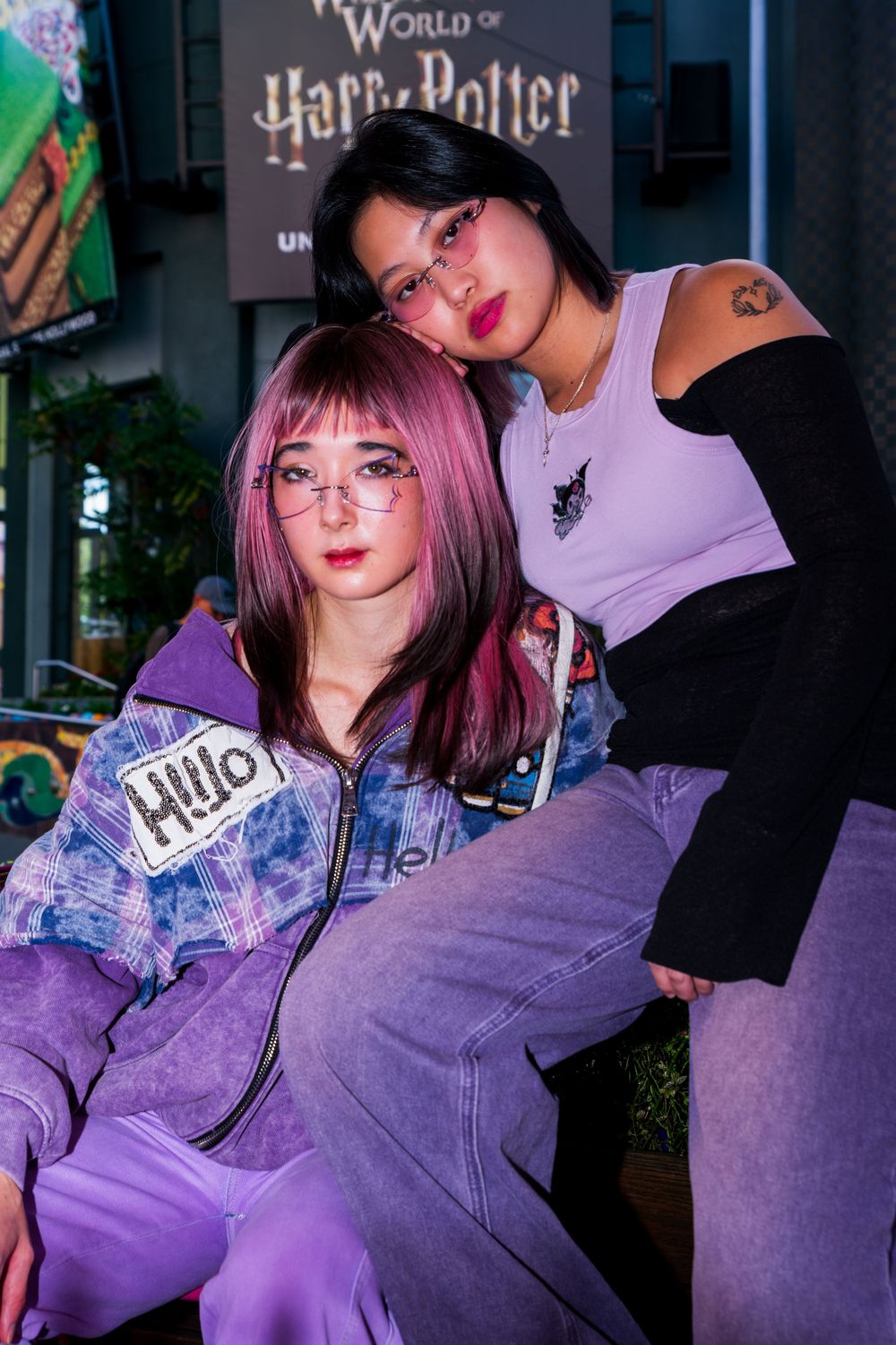 Person with pink hair and glasses poses in purple lighting wearing casual attire in a collage of similar photos.