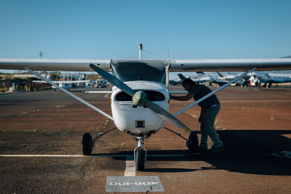 Row of small aircraft parked on desert airfield under clear blue sky.