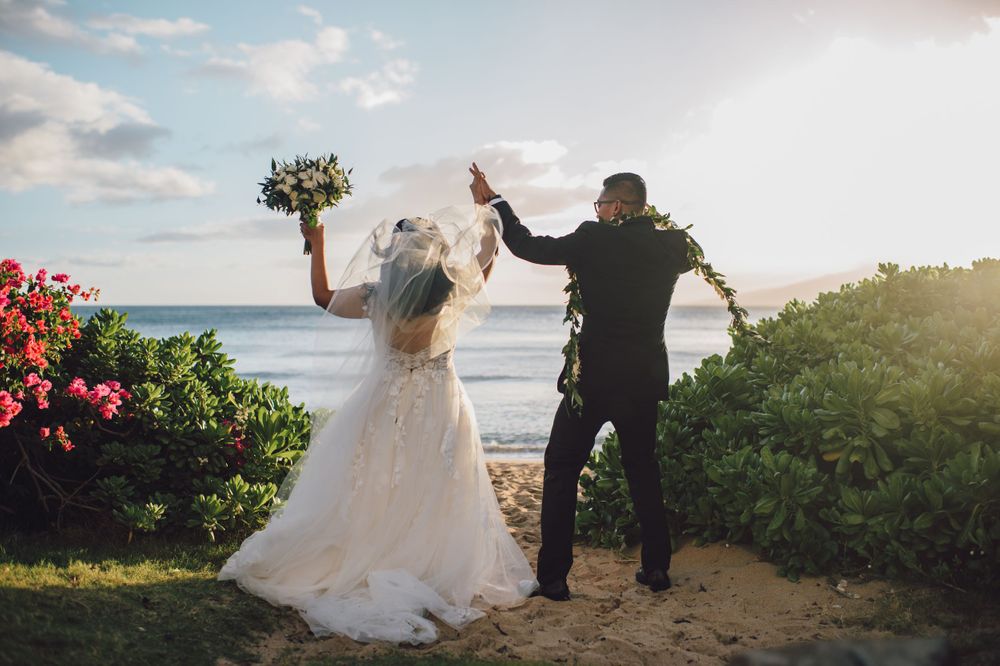 Joyful wedding celebration moment against ocean backdrop with red tropical flowers.