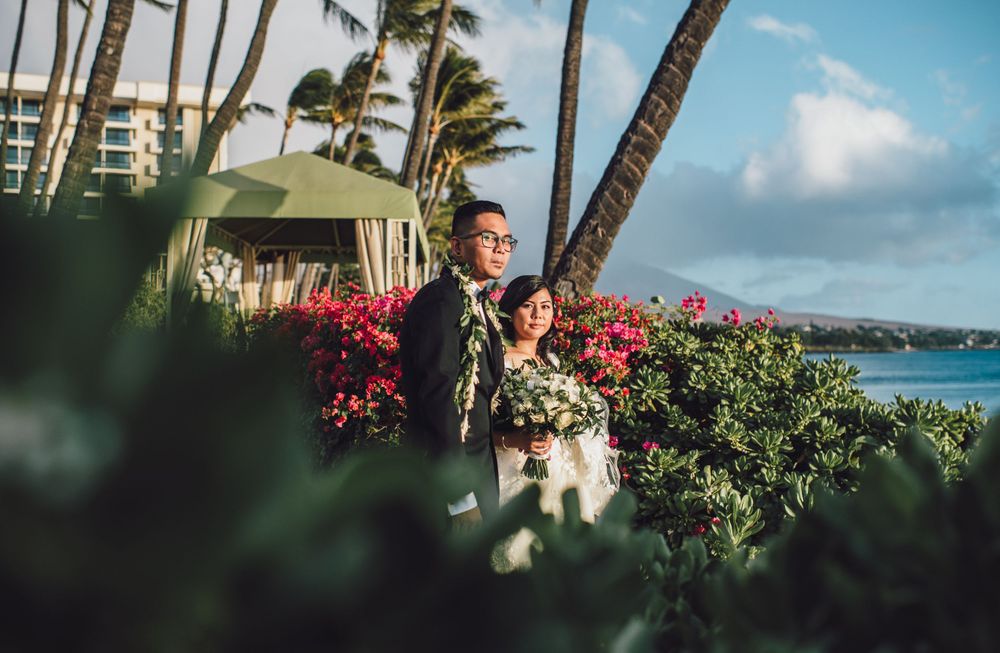 Tropical Hawaiian wedding scene with red flowers and palm trees against ocean backdrop.