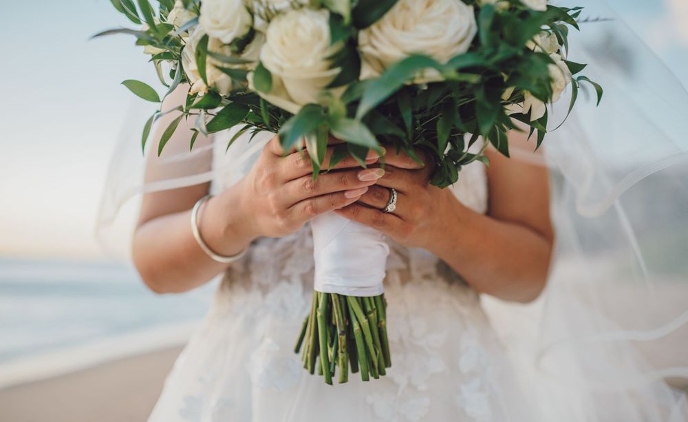Close-up of bridal bouquet with white roses and greenery held by hands showing wedding ring.