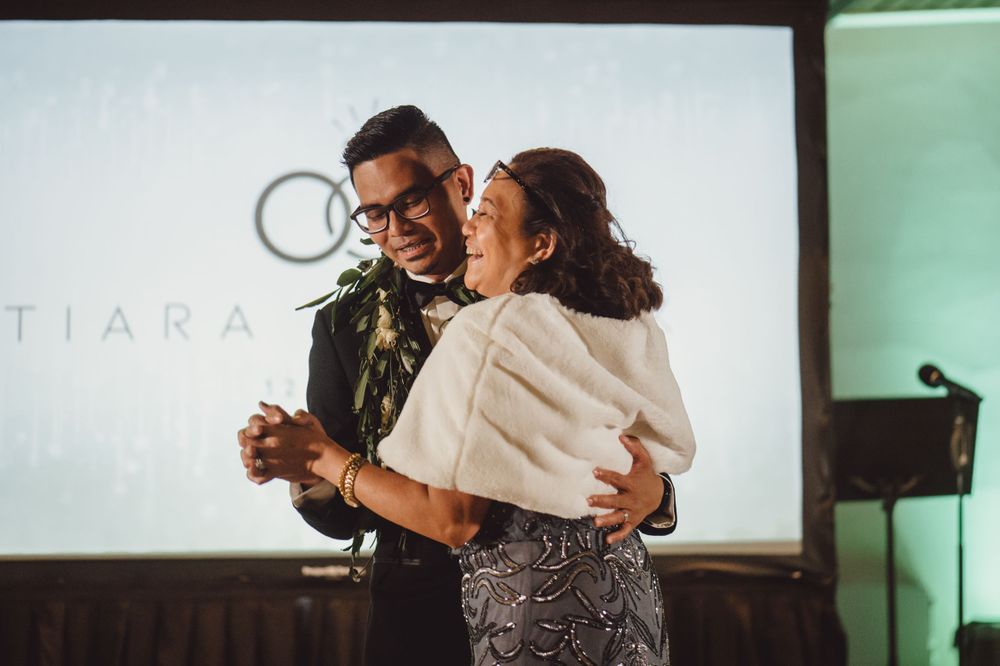 Couple dancing together at an indoor wedding reception with projection screen in background.