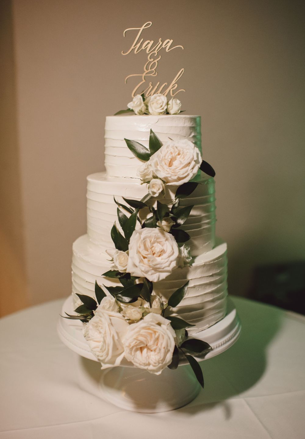 Elegant white wedding cake decorated with fresh roses and greenery.