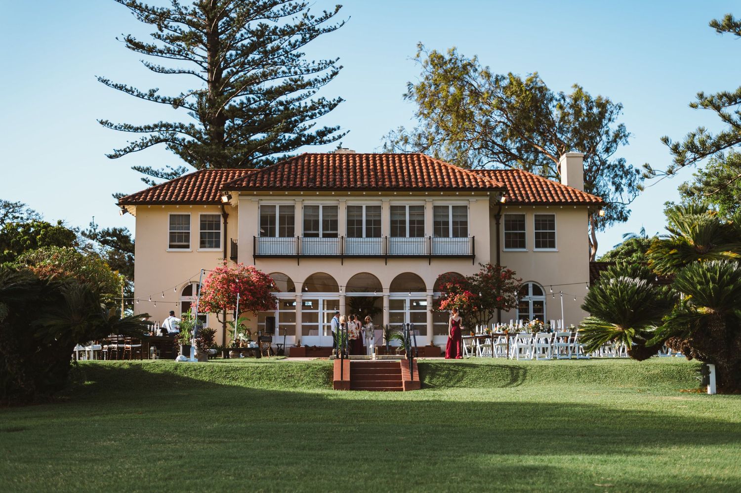 Panoramic view of a historic white mansion with red tile roof and manicured lawn.