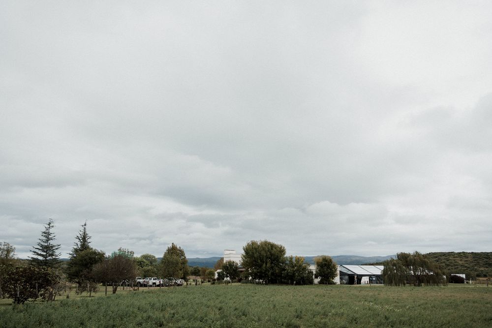 A panoramic view of a cloudy landscape with rolling hills, trees, and buildings scattered across the countryside.