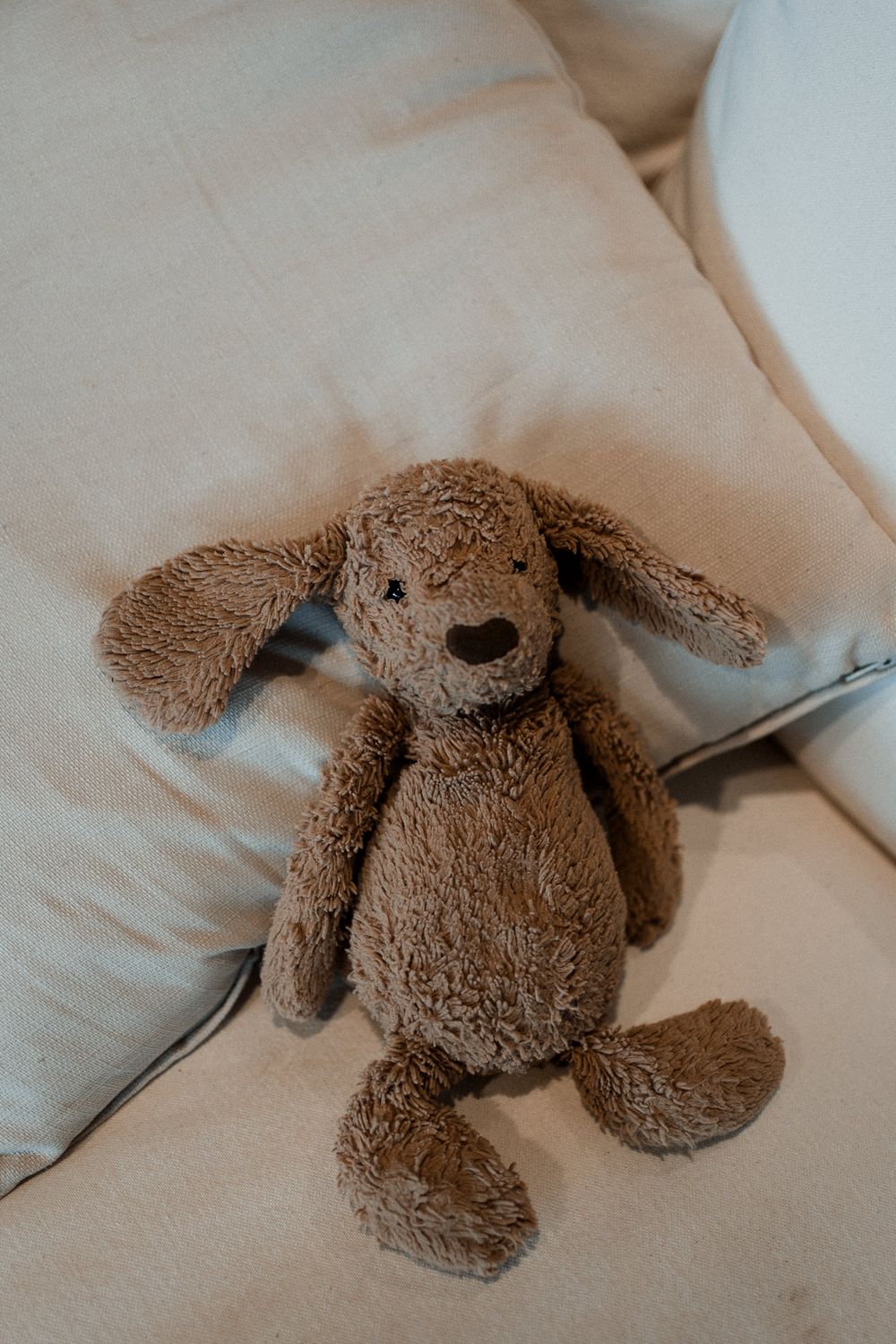 A brown plush dog toy lies on white bedding, shown from different angles in a sequence of photos.