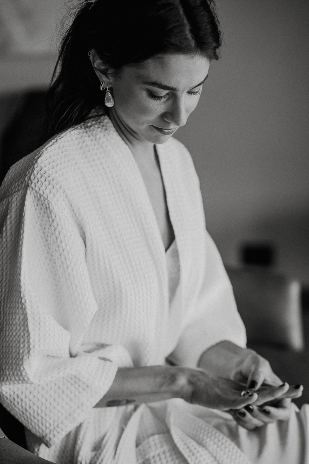 Woman in white bathrobe sitting while looking down at mobile phone in black and white photography series.