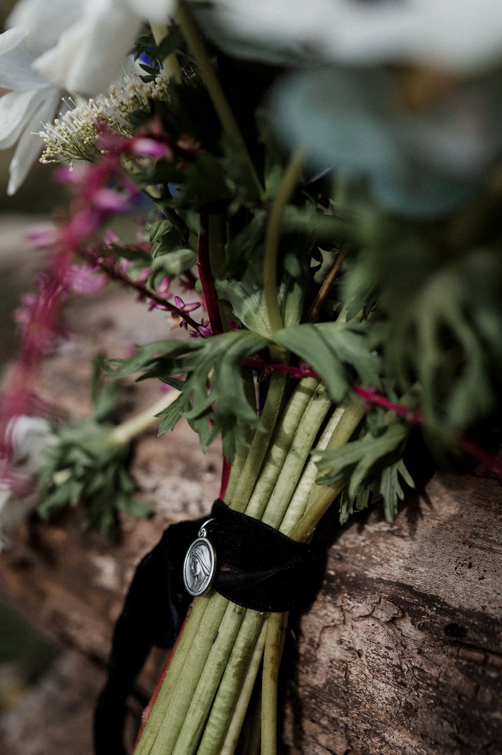 A bundle of fresh green asparagus stalks tied together with twine rests on a rustic wooden surface with pink flowers nearby.