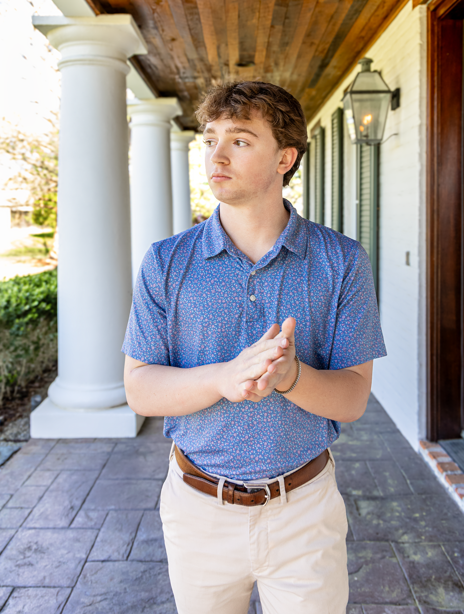 Young man in blue floral polo shirt stands on stone porch with white columns.