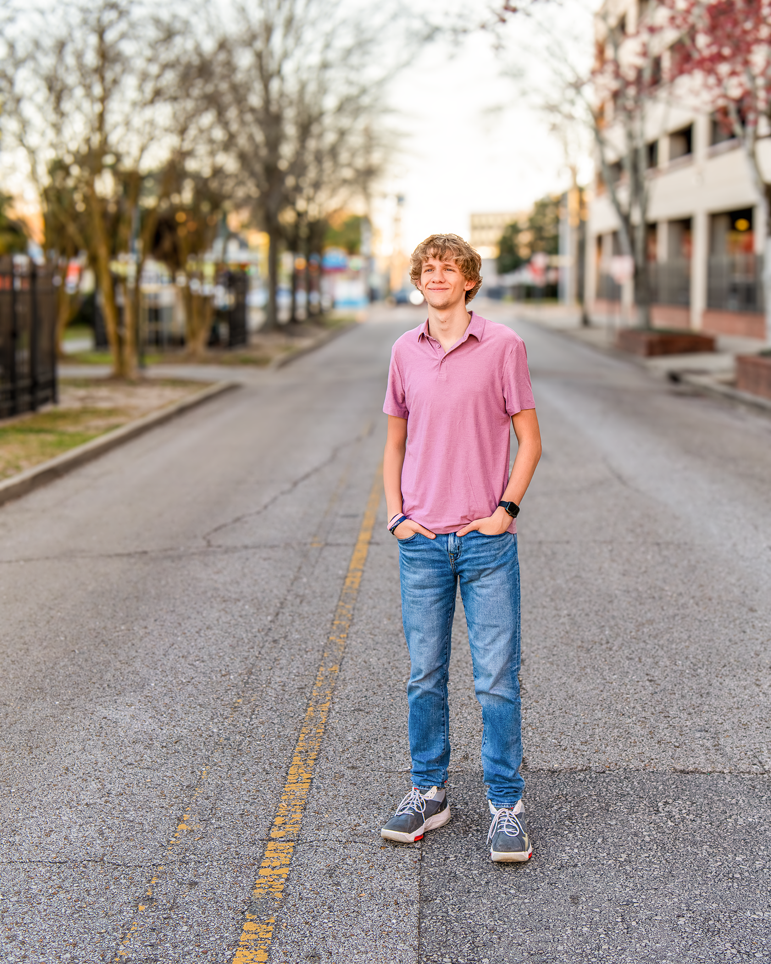 Teenage boy in pink polo and jeans standing on urban street centerline at golden hour.