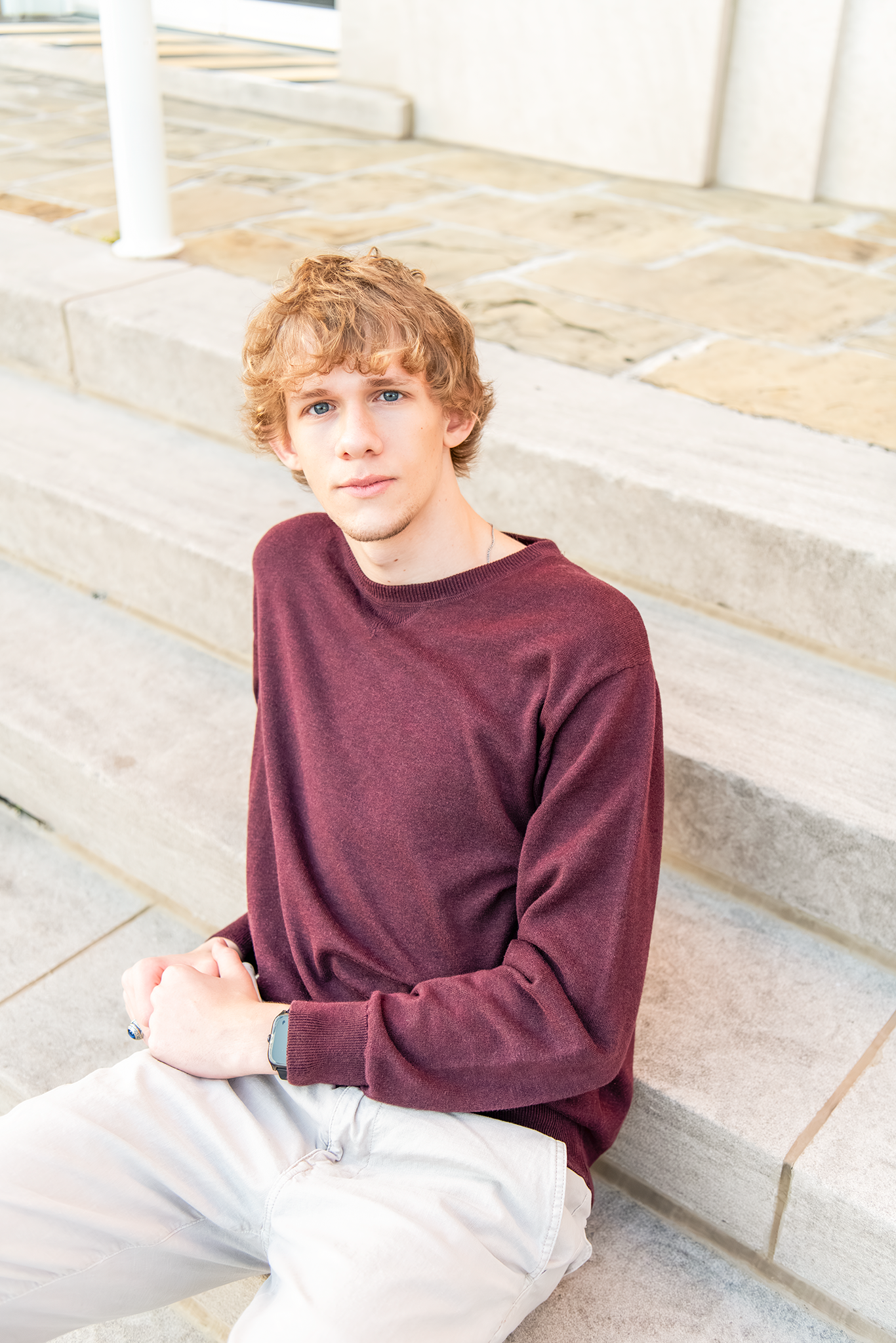 Teen boy in burgundy sweater sitting on stone steps for a senior portrait photo.