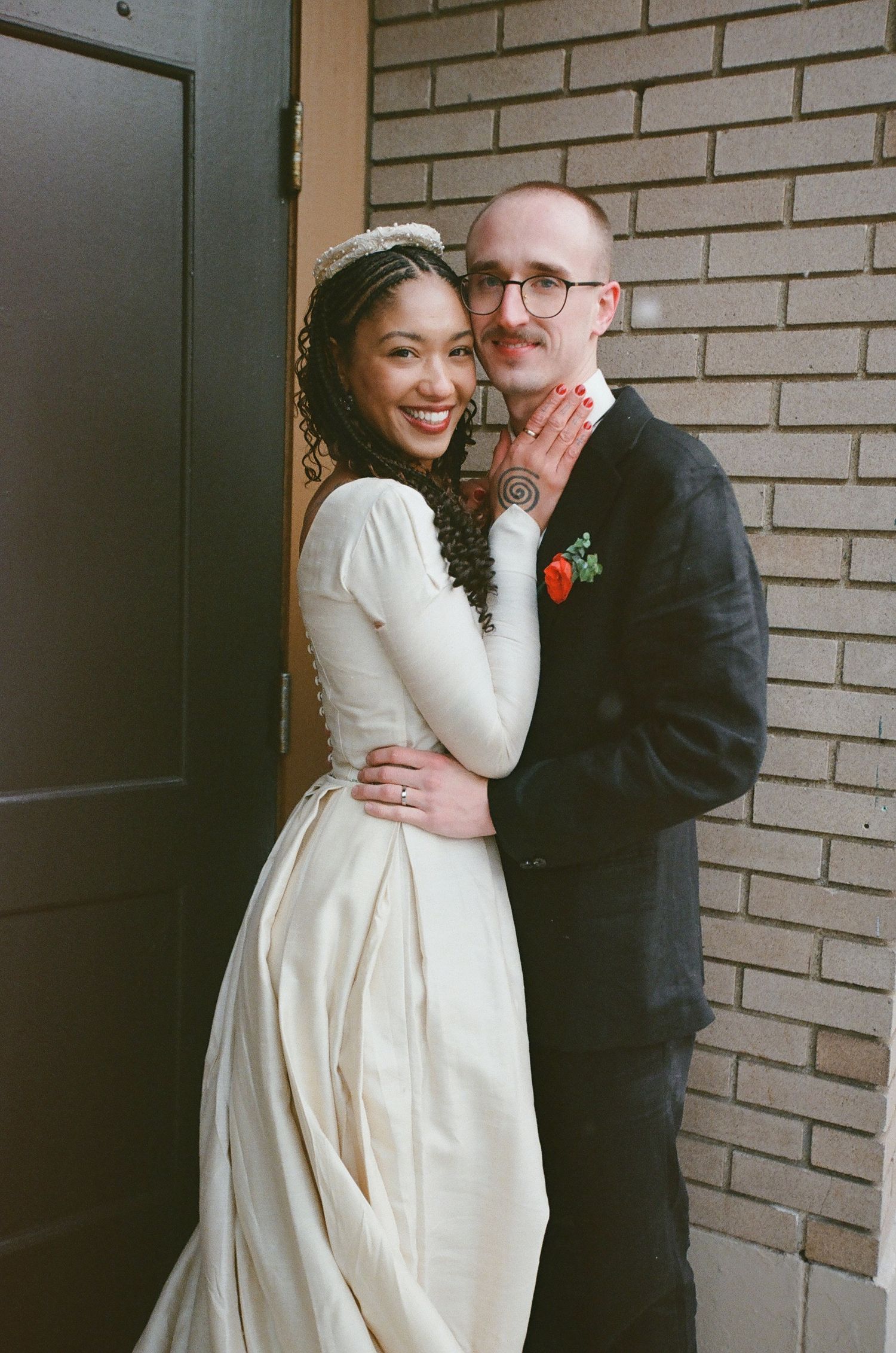 A romantic wedding couple embraces against a brick wall backdrop in an intimate moment.