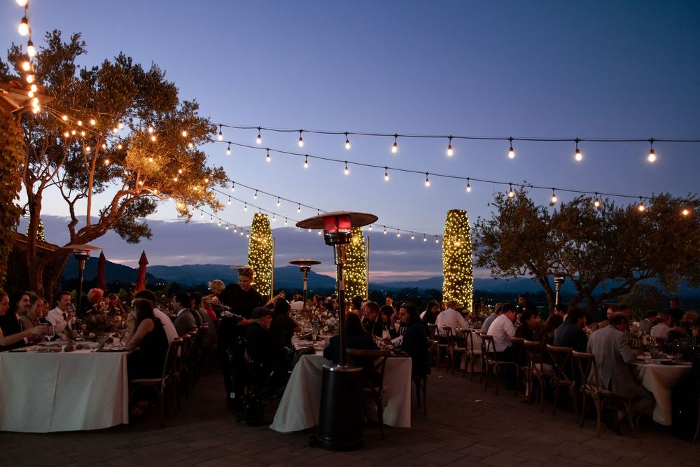 Outdoor wedding reception at dusk with string lights and illuminated tiki torches overlooking the ocean.