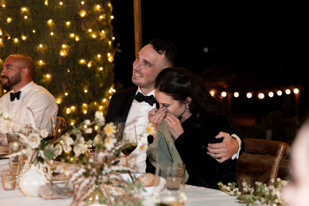 Couple shares an emotional moment at an elegant wedding reception with twinkling lights and floral centerpieces.