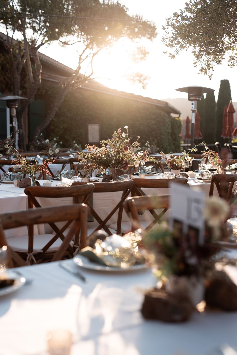 Outdoor wedding reception tables set with white linens and floral centerpieces at golden hour.