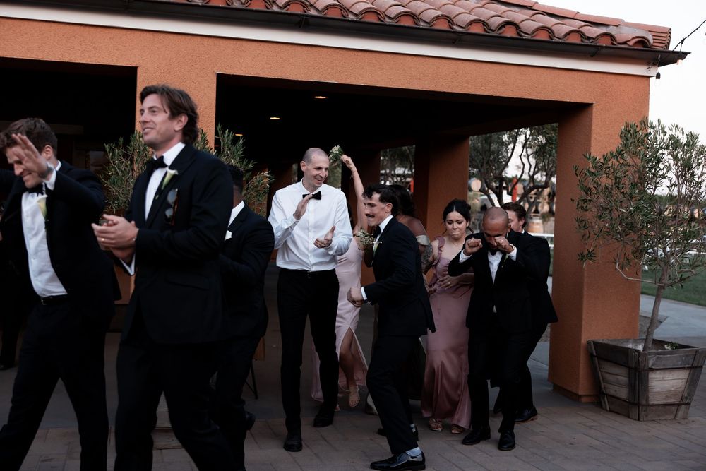 Formally dressed couples dance together in an elegant outdoor setting with terracotta roofing visible above.