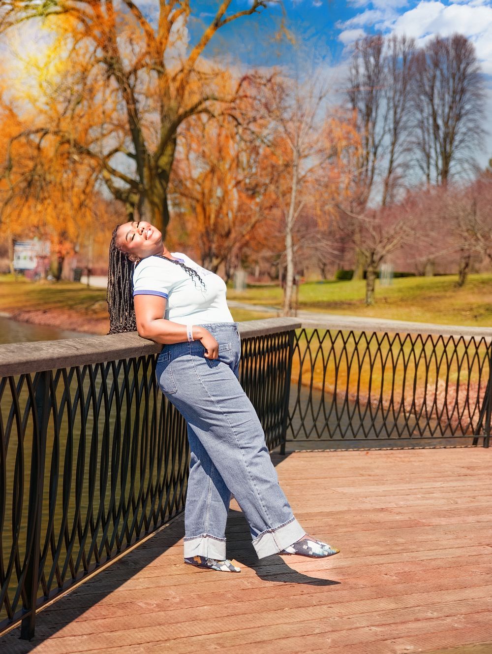 Woman in jeans and white top posing on a wooden bridge in a colorful autumn park on a sunny day.