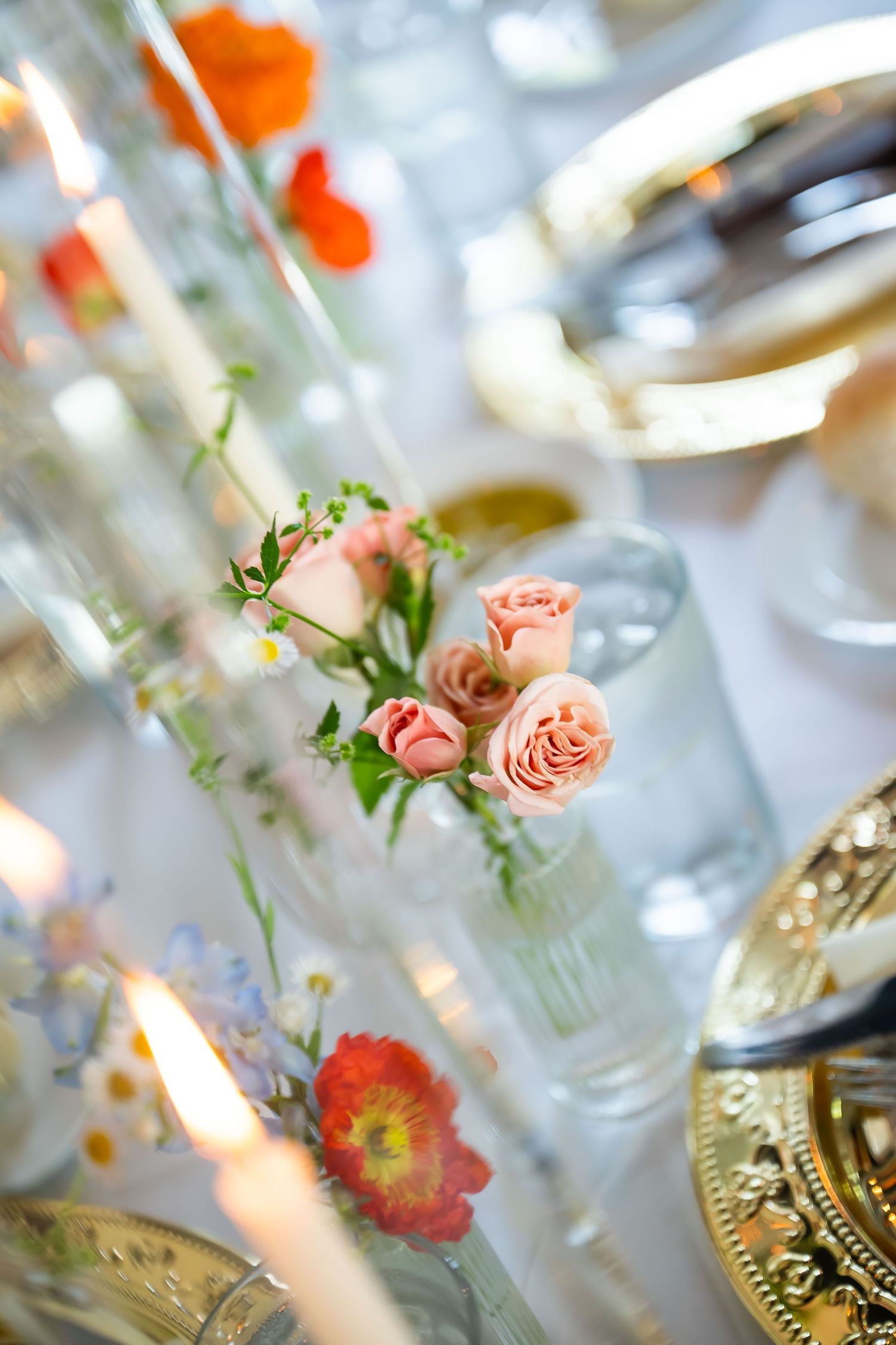 Elegant wedding table setting with pink roses in glass vases, candles, and gold charger plates.