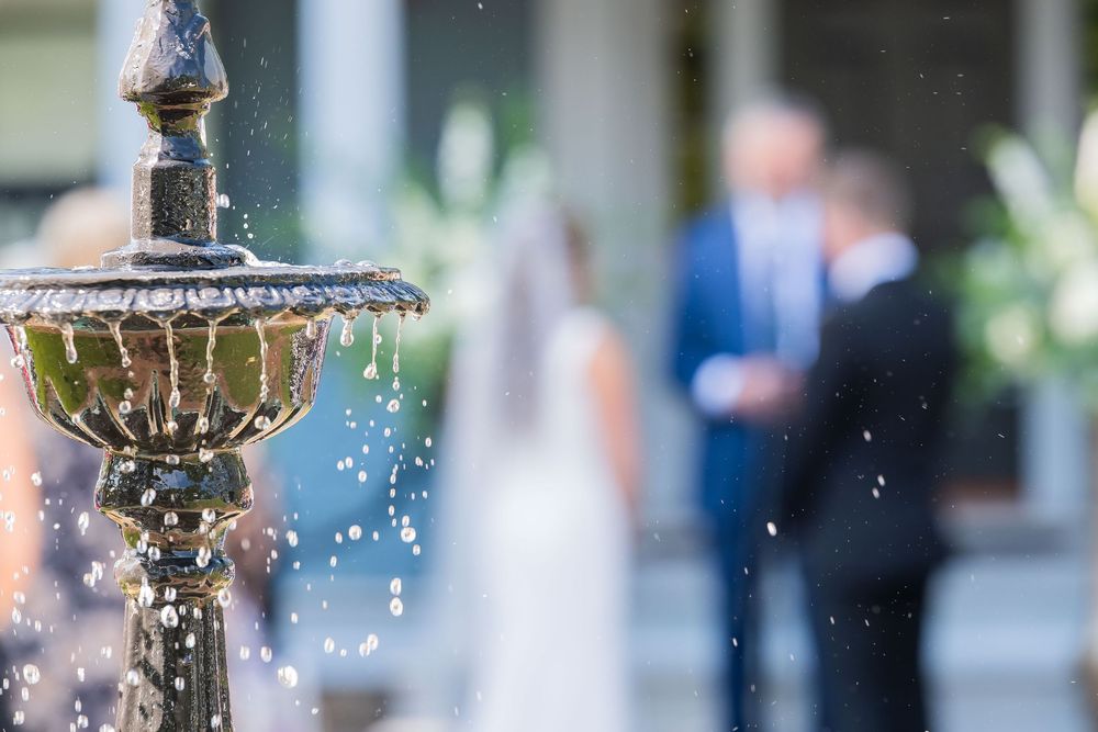 An ornate stone fountain sprays water droplets with a soft blurred background of a garden event.