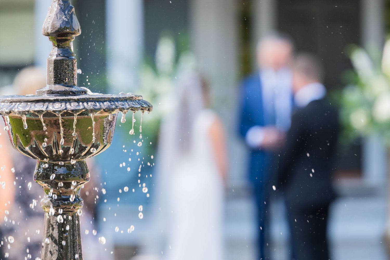 An ornate stone fountain sprays water droplets with a soft blurred background of a garden event.