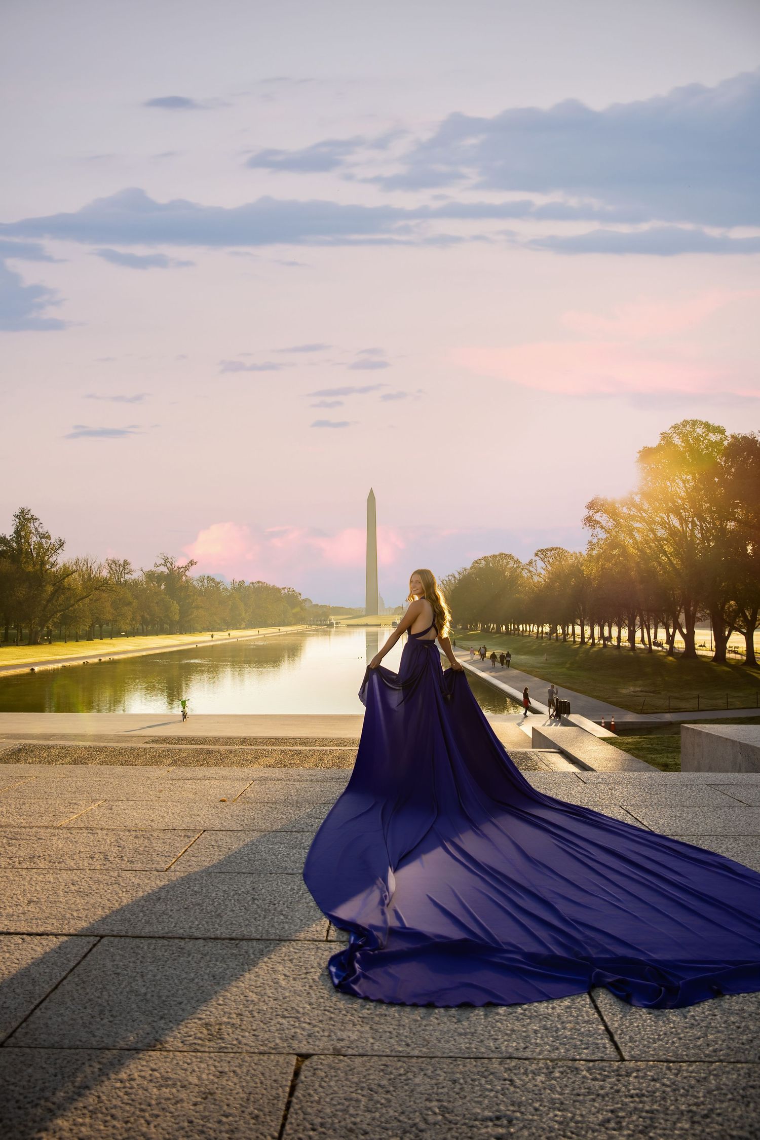 Figure in flowing navy blue gown poses at Lincoln Memorial Reflecting Pool during golden sunset in Washington DC.