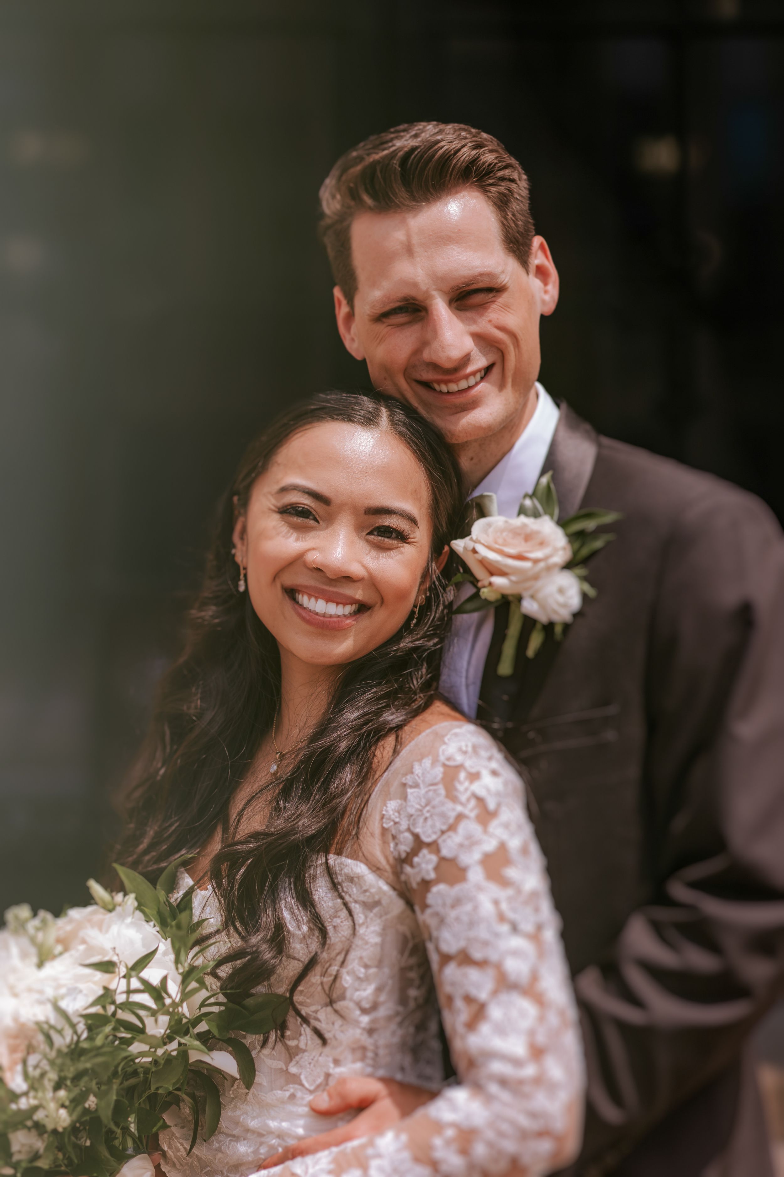 A couple shares joyful laughter during their wedding day, wearing traditional white lace dress and dark suit.