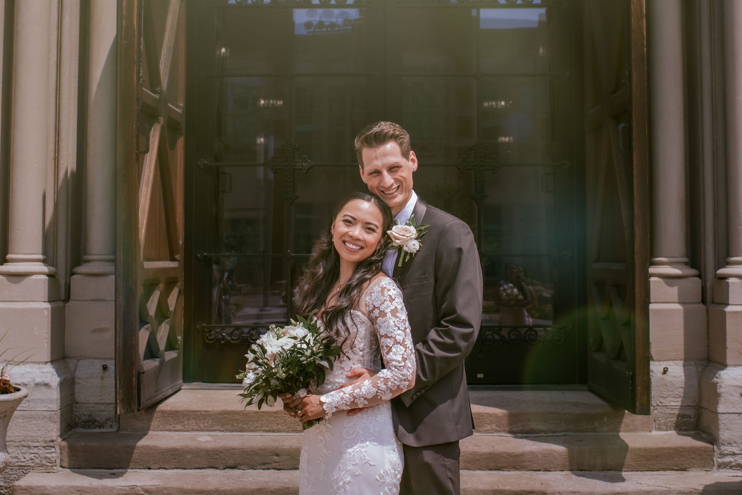 Elegant bride and groom pose together in a classic stone archway with romantic lighting.