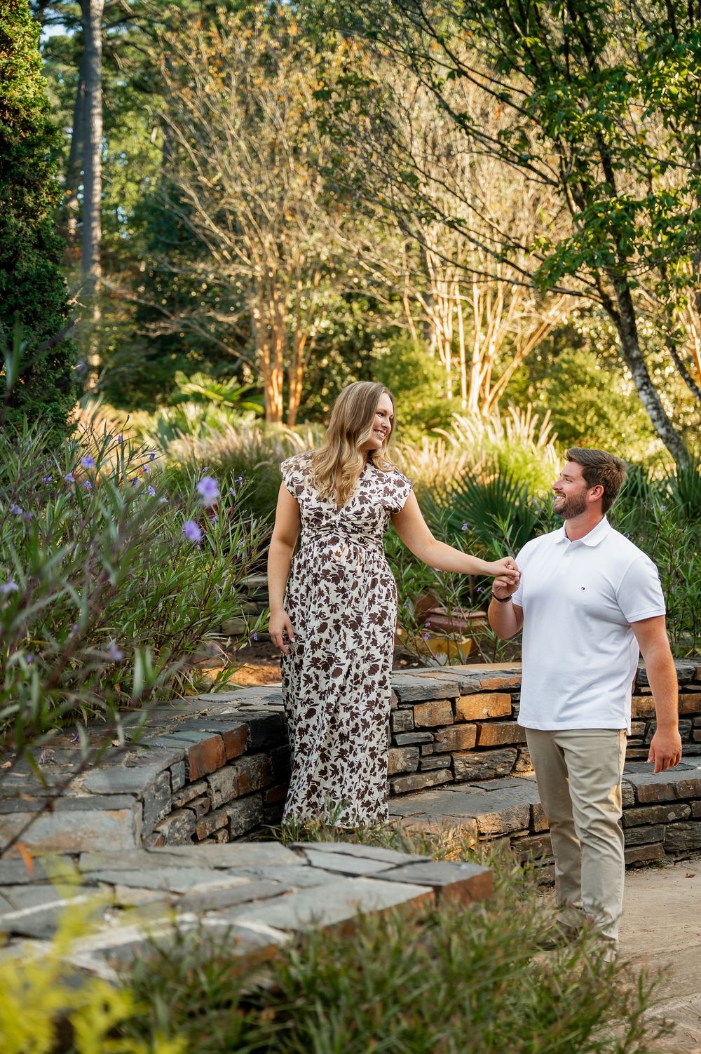 Couple shares tender moment while sitting on stone wall in landscaped garden.