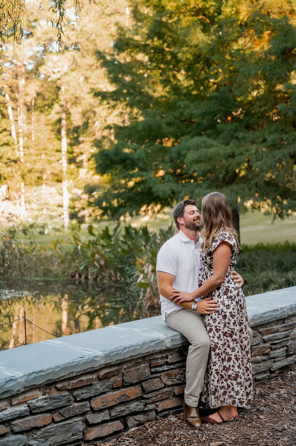 Romantic couple sits close together on stone wall surrounded by autumn foliage.