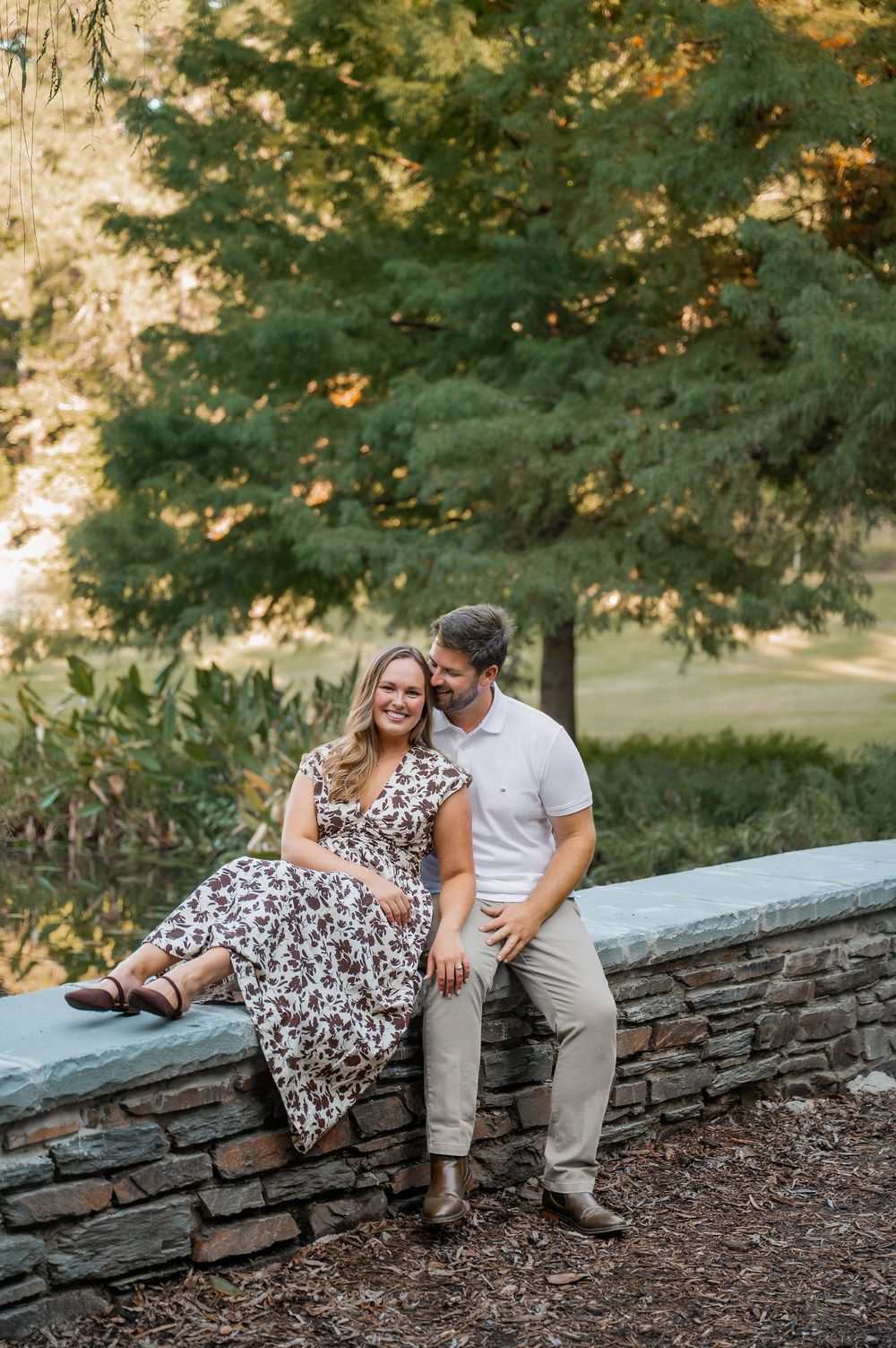 Couple shares intimate moment while sitting on stone wall in garden setting.