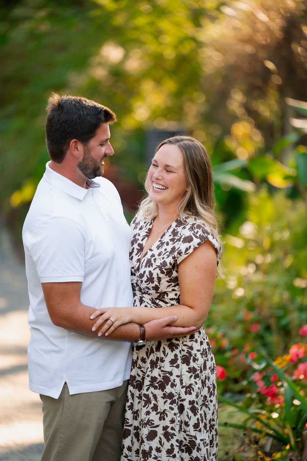 Couple shares joyful laughter while embracing in a garden with vibrant flowers.