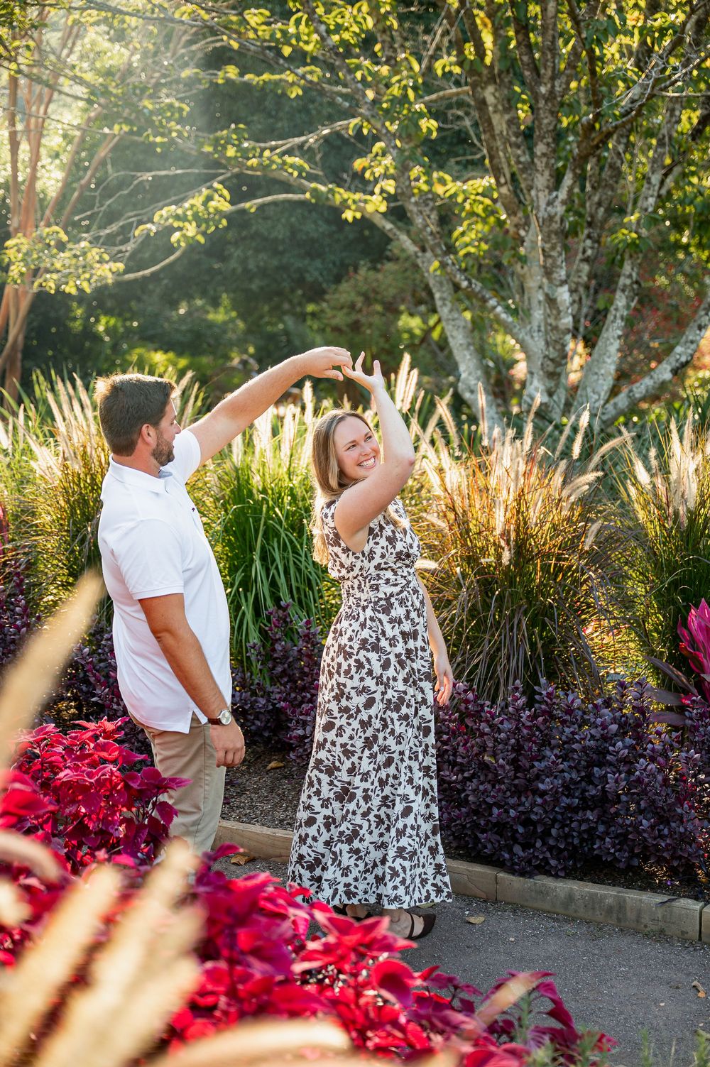 Dancing couple enjoys romantic moment among colorful garden flowers at golden hour.