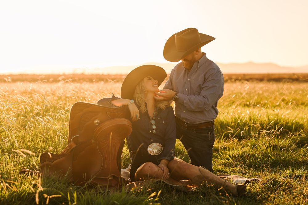 A couple sits together on a grassy hill during golden hour sunset, creating a romantic silhouette against the warm sky.