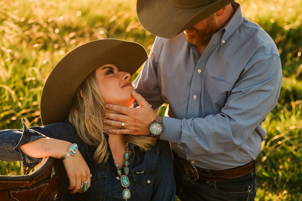 Romantic couple embracing in golden sunlight wearing western style clothing and hat.