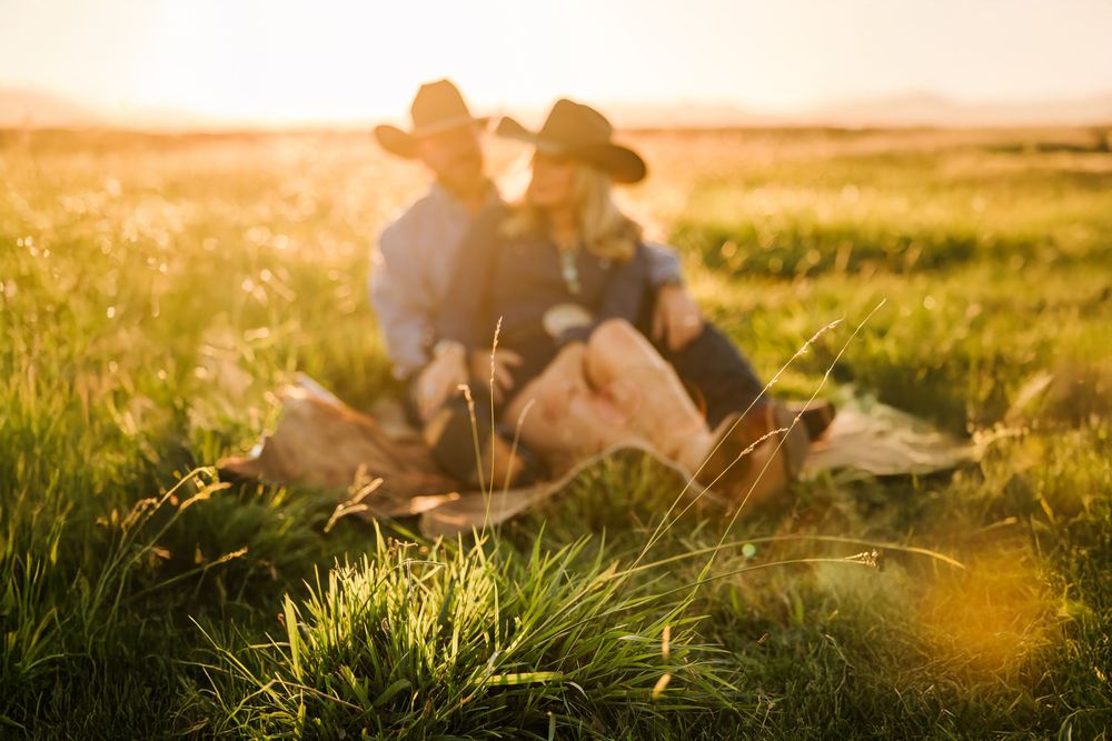 A silhouette of a couple sits in a grassy meadow during golden hour sunset creating a romantic atmosphere.