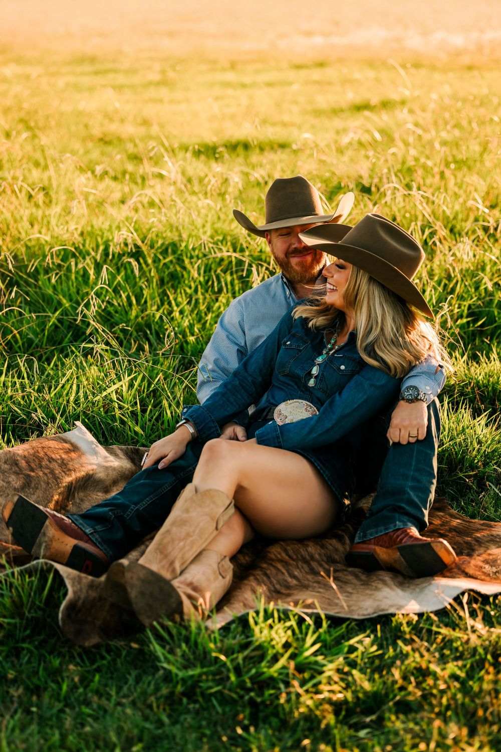 A couple in western attire relaxes together on grass during golden hour sunset.