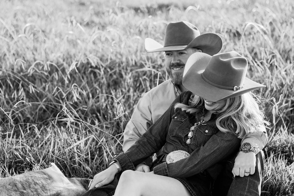 Couple in cowboy hats laying together in a sunlit grassy meadow.