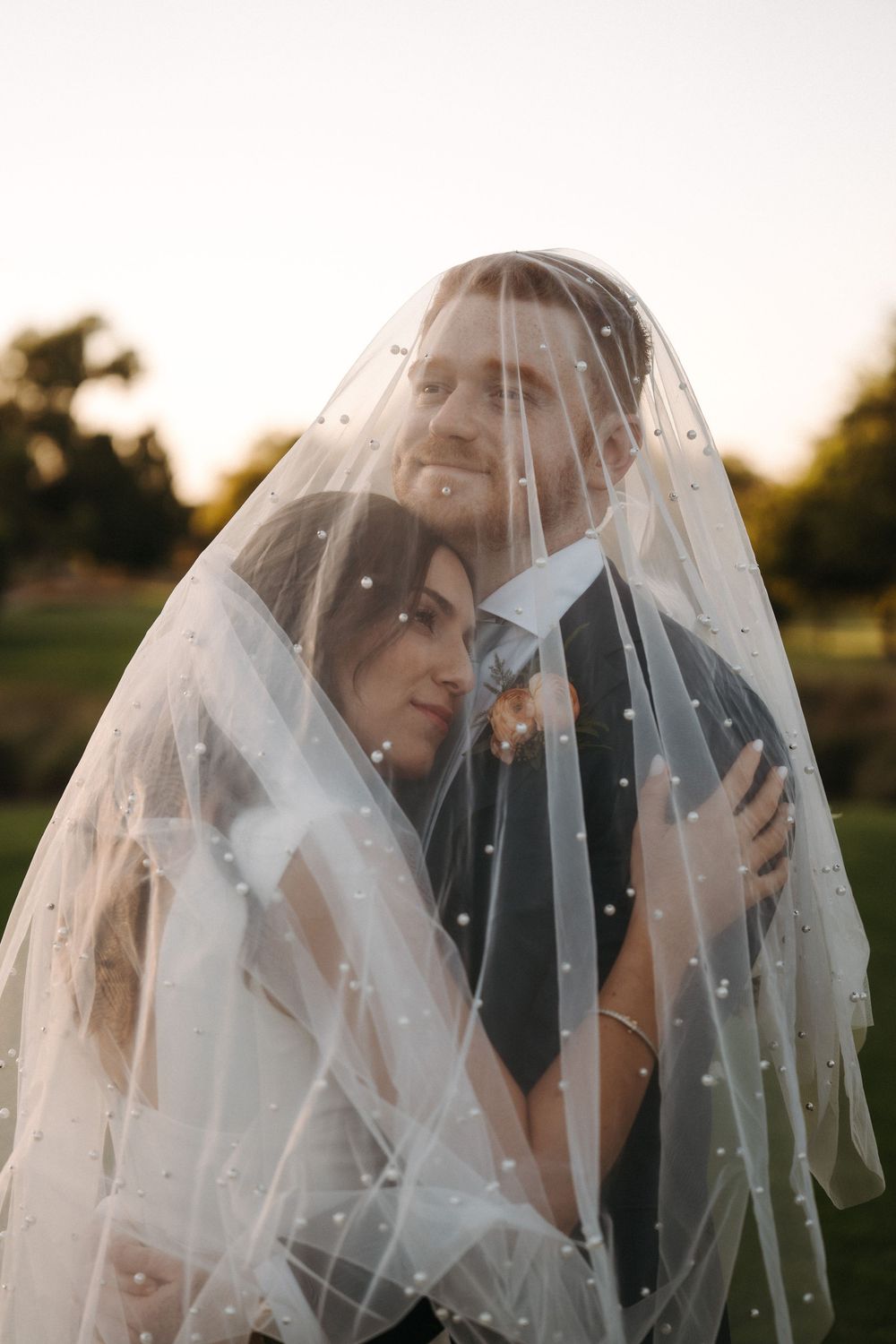 A romantic wedding portrait series showing a couple sharing intimate moments under a delicate white veil at sunset.